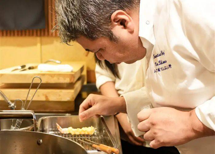 Chef Shimura Koichiro sprinkling seasoning on freshly fried tempura.